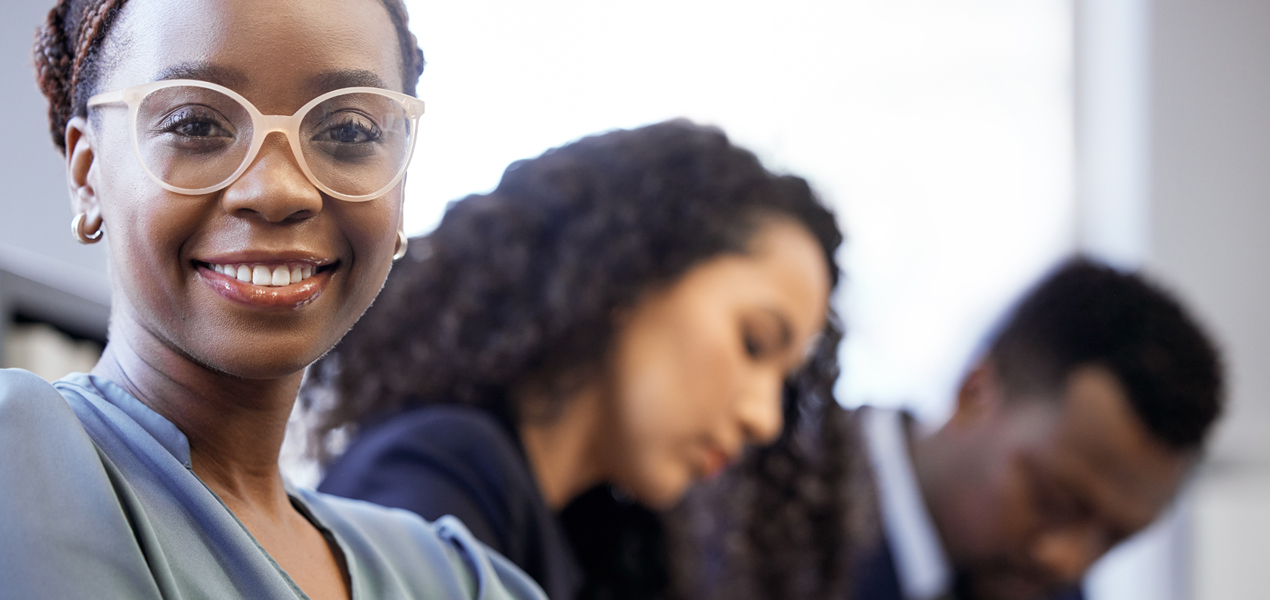 A young black business woman smiling at the camera while sitting with her colleagues in the boardroom.