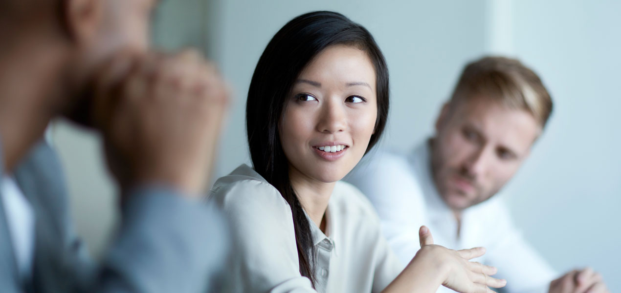  Two men listening to a woman speaking during a meeting.