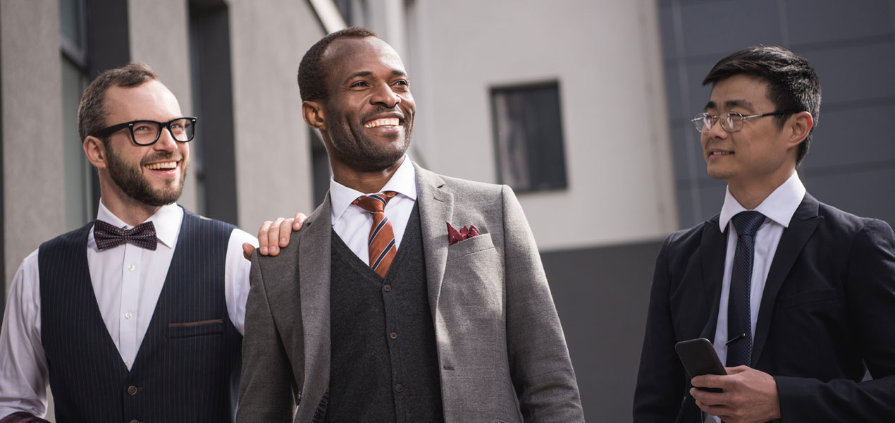 Three diverse men in formal wear laughing and chatting while walking.